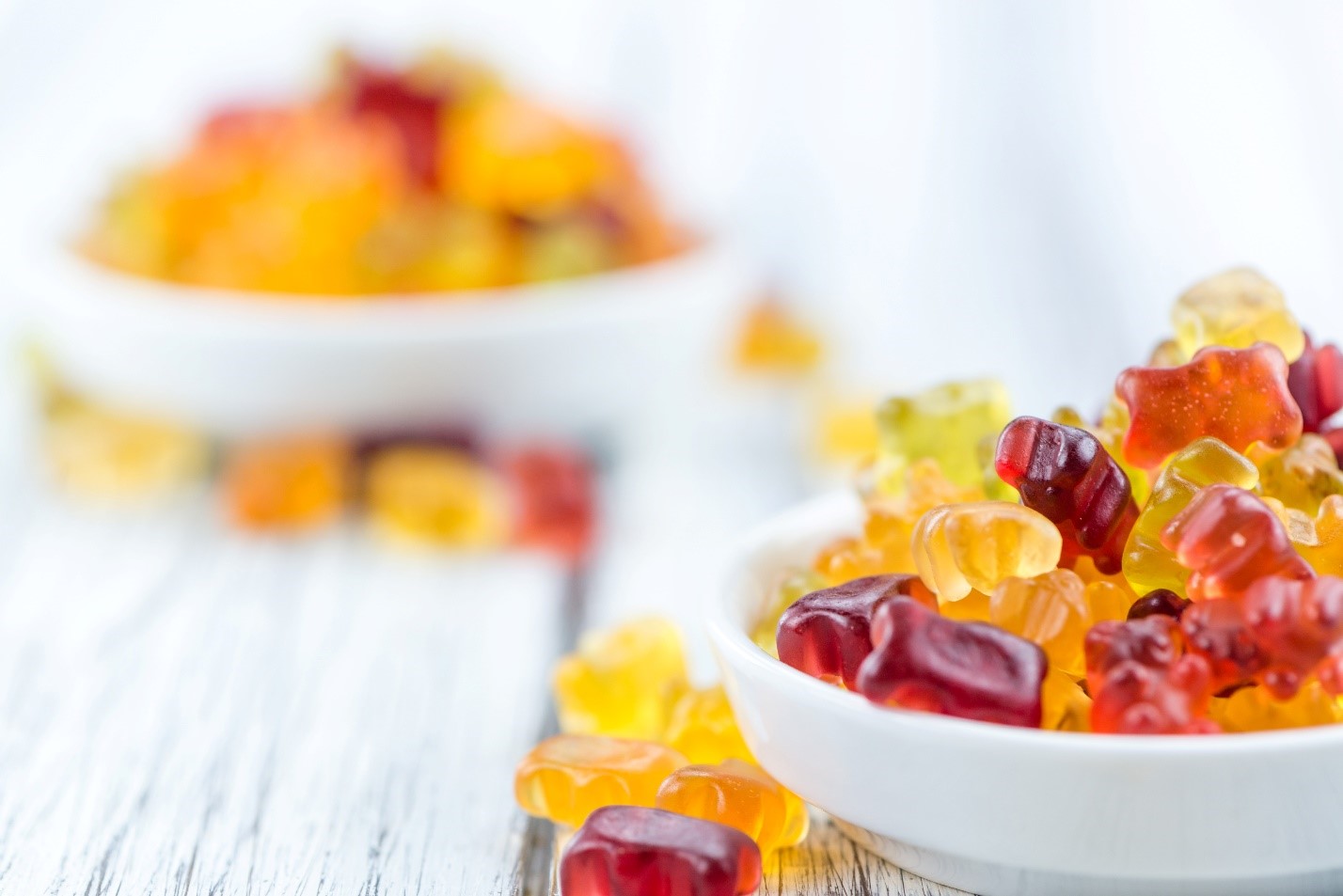 A bowl of gummy bears on white wooden background