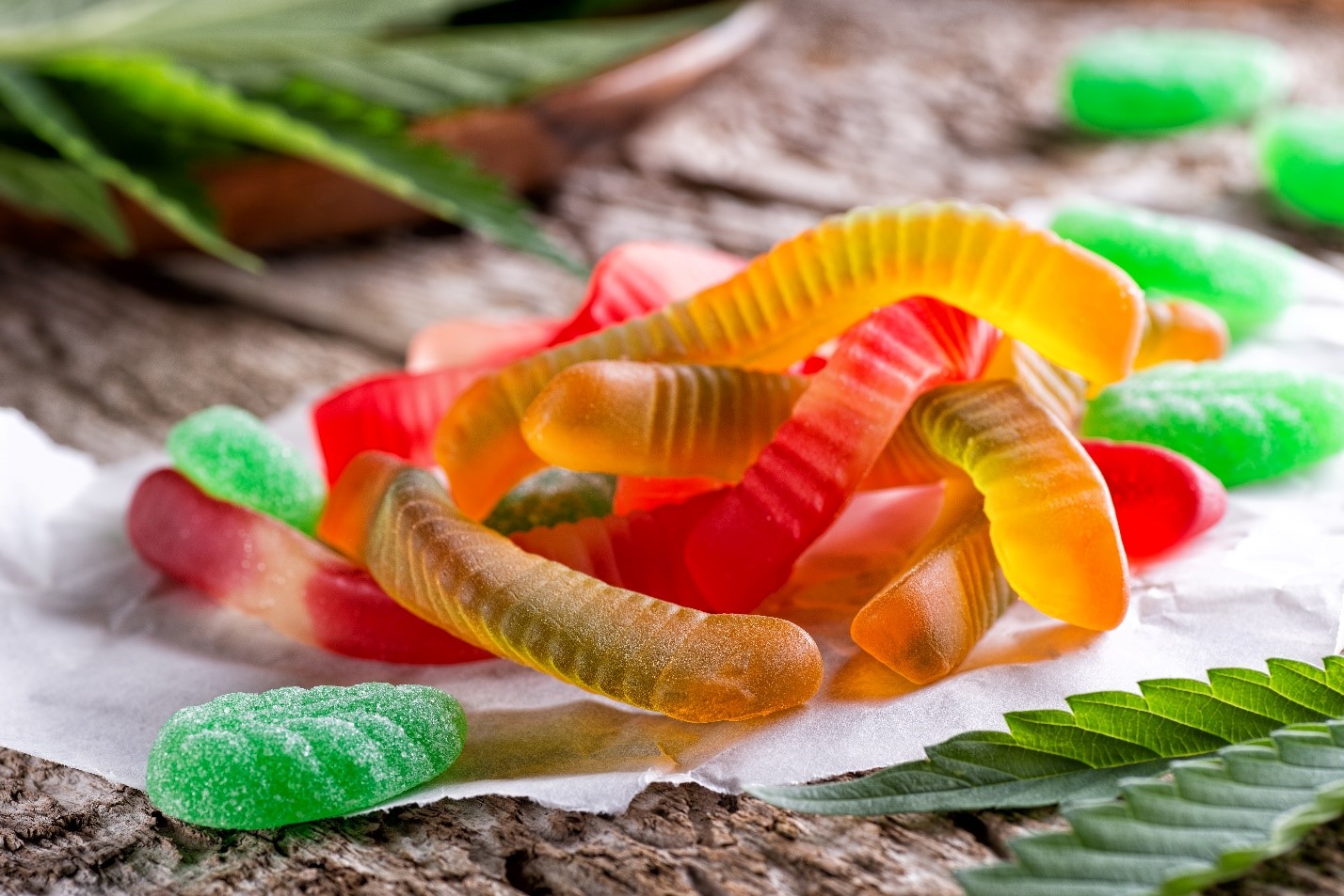 Hemp leaves and CBD infused gummy candies on wooden table