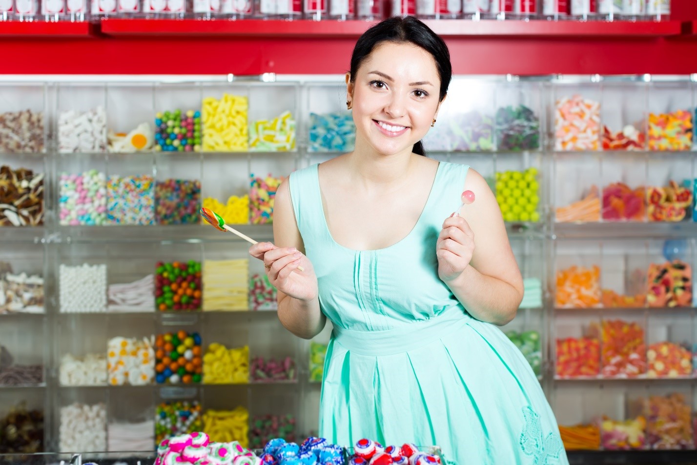Young woman posing with a lollipop in front of a display in a candy shop